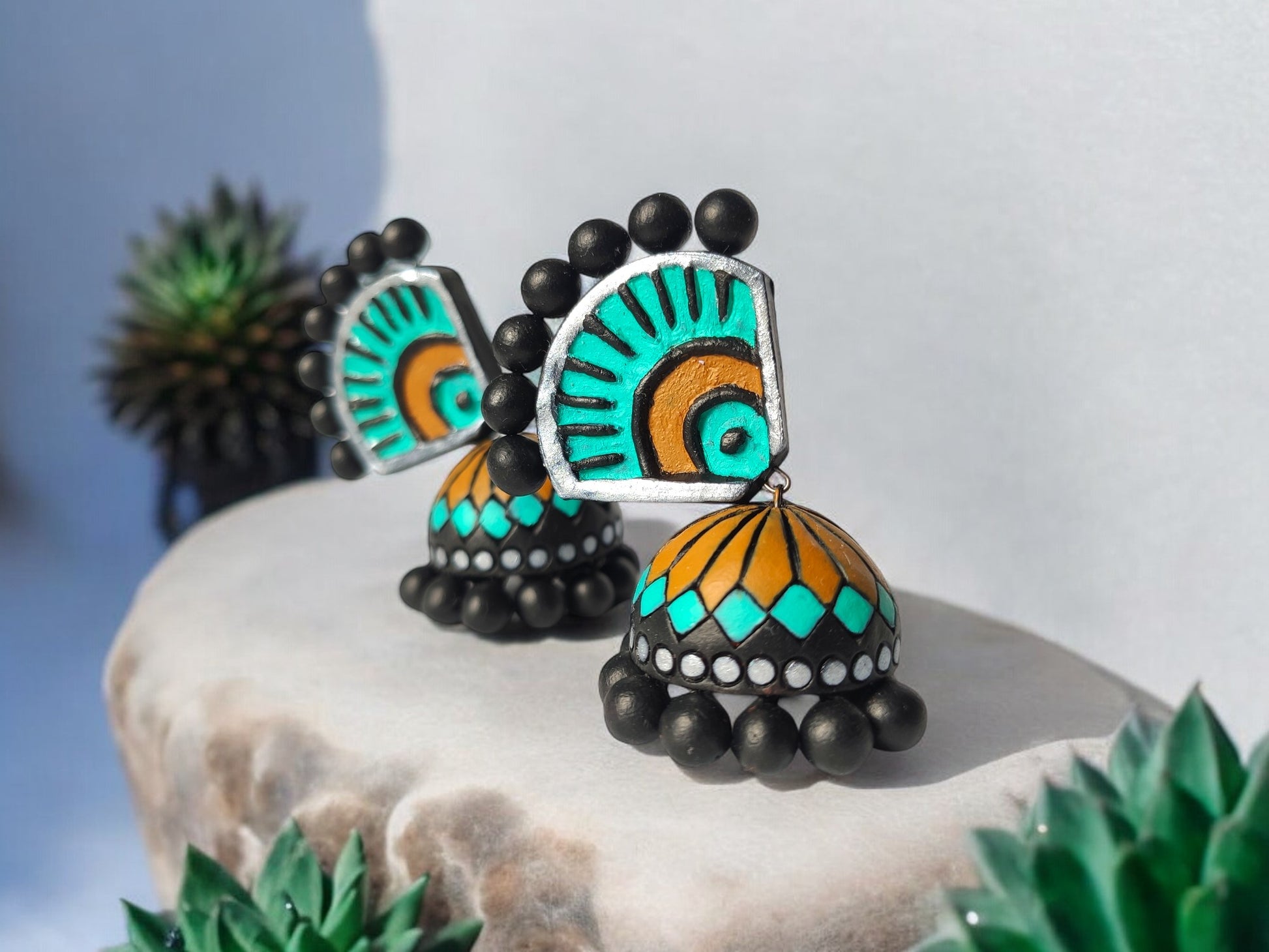 Experience the luxury of the Aachal Terracotta Jhumka, adorned with a captivating blend of teal blue, mustard yellow, and bold black. These handcrafted jhumkas, made from premium terracotta, add a touch of sophistication and elegance to any outfit, making it an exclusive must-have accessory.

